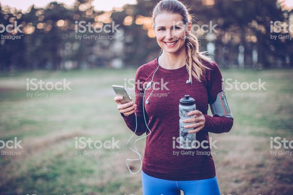 Young woman jogging outside at park. She took a break to rest. Holding her smart phone and headphones.